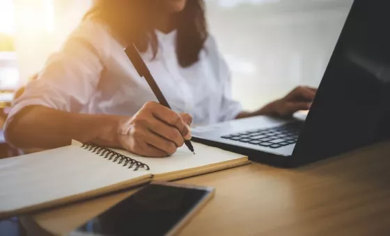 Une femme devant son ordinateur qui prend des notes sur un cahier