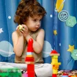 Enfant assis jouant avec des jouets colorés devant un rideau décoré d'étoiles et planètes