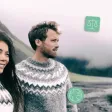 Un couple en pulls traditionnels observe la côte volcanique islandaise sous un ciel brumeux