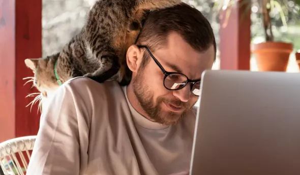 jeune homme devant un PC avec un chat sur l'épaule