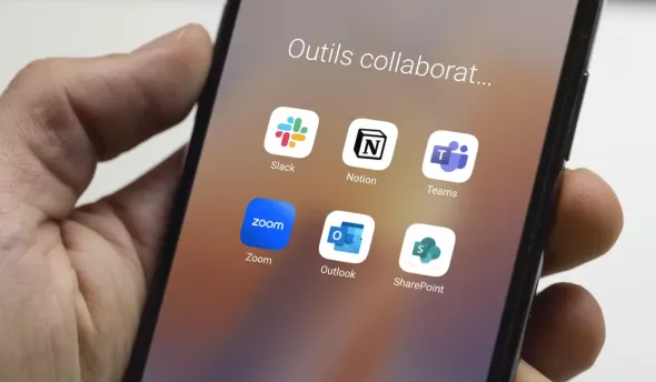 main qui tient un téléphone mobile avec un écran montrant des applications d'outils collaboratifs