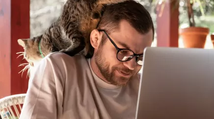 jeune homme devant un PC avec un chat sur l'épaule