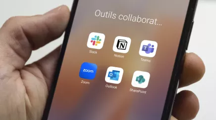 main qui tient un téléphone mobile avec un écran montrant des applications d'outils collaboratifs