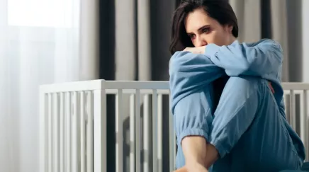 jeune femme pensive assise devant un lit de bébé