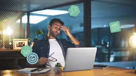 Un salarié fatigué assis devant un ordinateur, se frottant les yeux au bureau