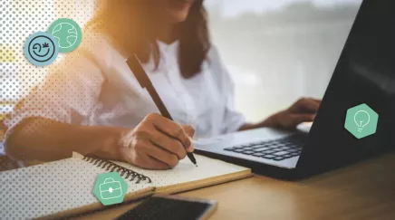 Une femme devant son ordinateur qui prend des notes sur un cahier